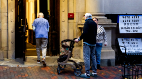 Older voters enter a poll site, one using a walker-style mobility assistance device.