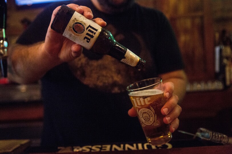 A bartender empties a beer bottle into a pint glass
