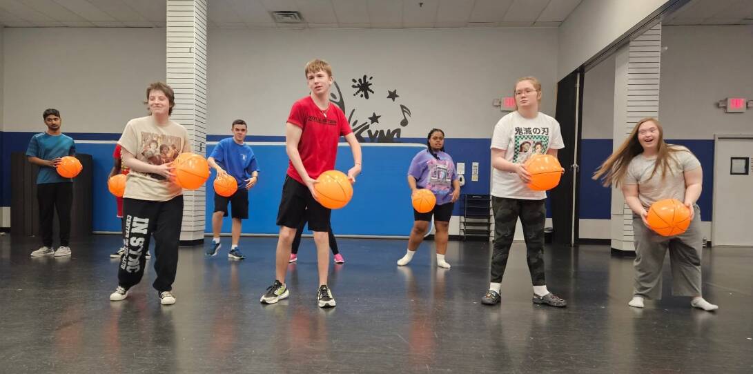 A group of young dance students each holding an orange inflatable ball.
