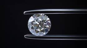 A pair of tweezers hold onto a cut diamond.