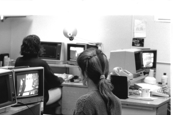 A black and white photo shows an open office, where several caption writers sit at their workstations.
