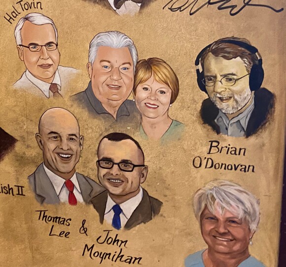 this is a photograph of one of the walls at The Palm restaurant in Boston. Their walls are legendary for having caricatures of locals. this second of the wall features a cluster of seven people. all of the illustrations are essentially head shots. Among the group is Brian O'Donovan, who is clearly in broadcast as he is the only persona illustrated wearing headphones.
