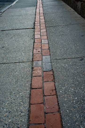 Two rows of bricks in the center of a sidewalk stretch the distance of the visible path.