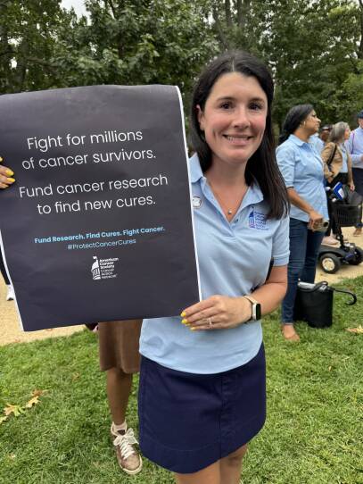 A woman holds a sign that says "Fight for Millions of Cancer Survivors - Fund cancer research to find new cures."
