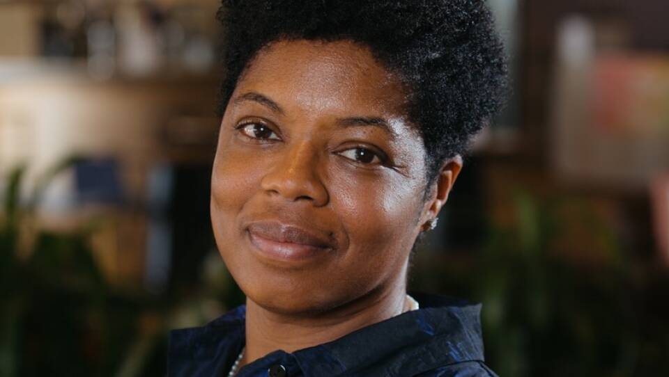A close-up photo of a Black woman with dark-colored shirt smiling at the camera.