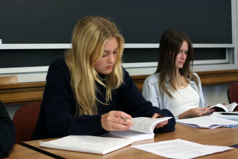 A woman with long hair and a black shirt peers down at an open book in her hands.