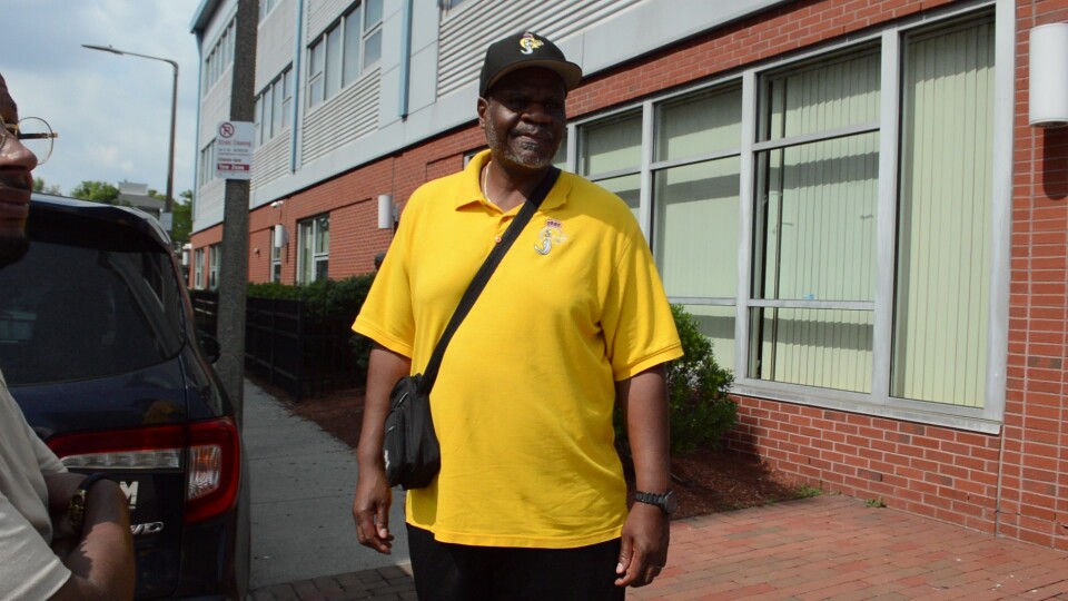 A man in a bright yellow polo shirt stands on the street. 