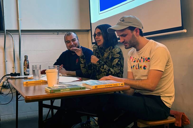 Three people sit at a table, with comic books in front of them.