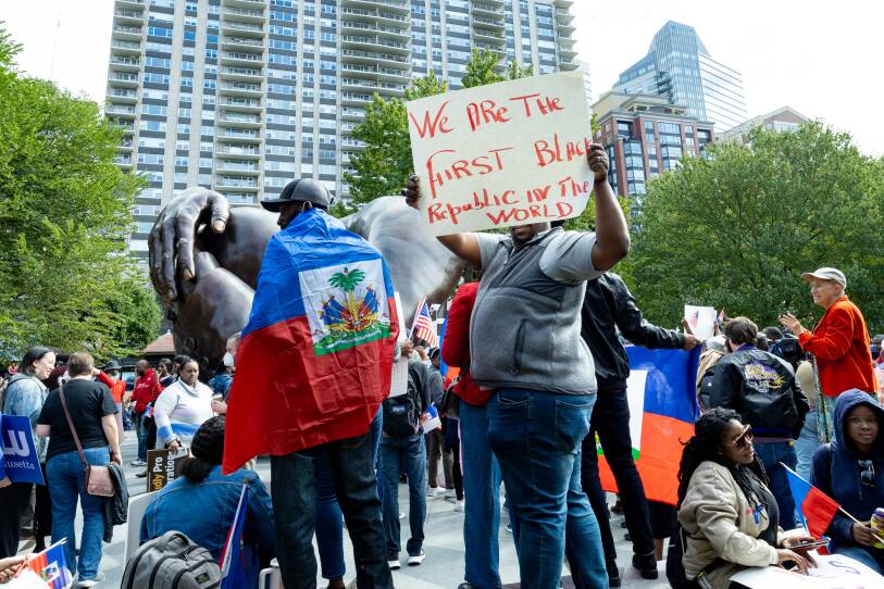 A person holds a handmade sign that says "We are the first Black republic in the world" while standing in a crowd in a public park.