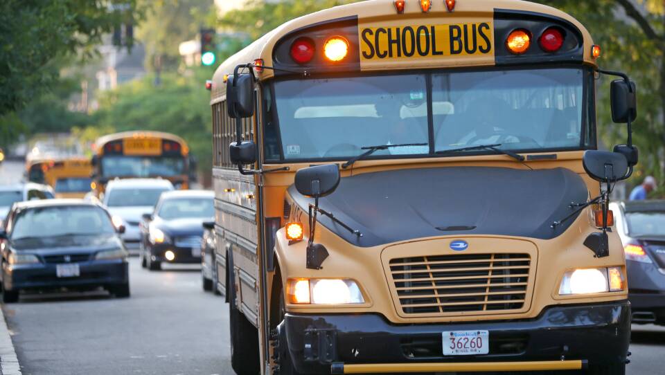 A school bus goes down a busy Boston street, with two school buses visible behind it