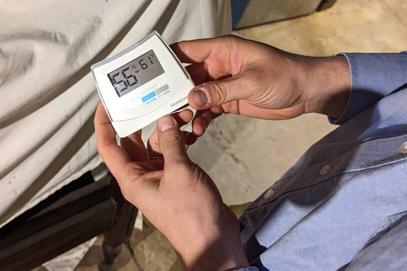 A person holds a small rectangular device that looks like a digital thermostat, reading 56% relative humidity and 61 degrees fahrenheit.