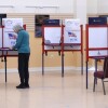 A person stands at a polling booth set up in a large room.