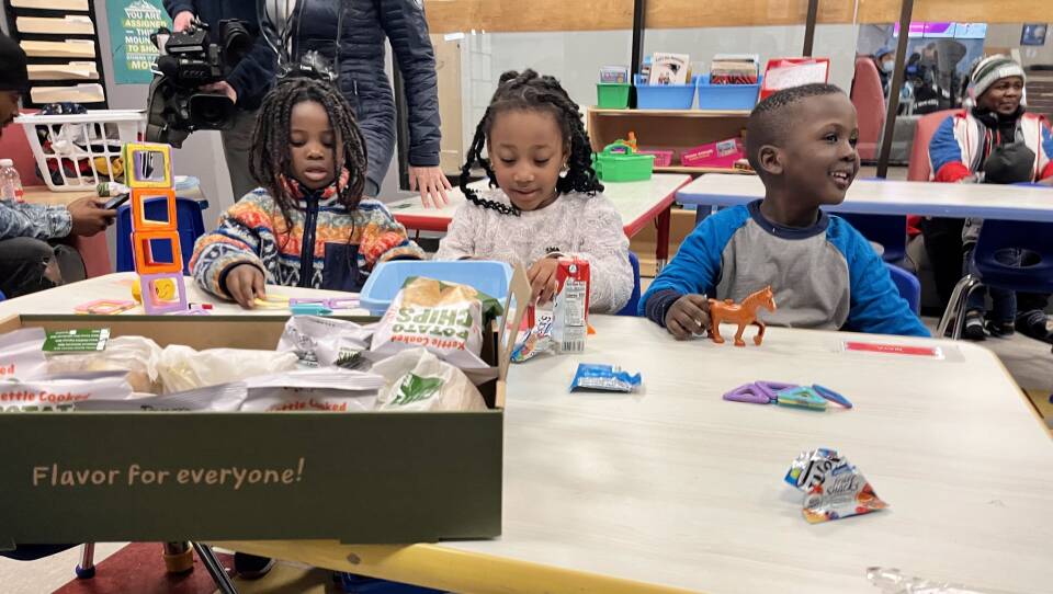 Three young Black kids sit at a table, playing with toys.