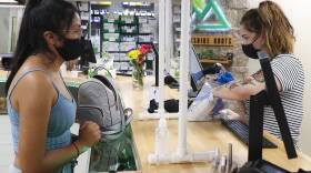 A woman stands at a wooden counter with her backpack next to her. Another woman on the other side of the counter uses a computer to complete a purchase.