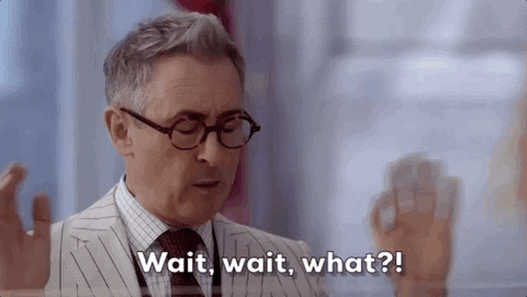 A man in a white pinstripe suit and round horn-rimmed glasses shakes his hands and head and says "wait, wait what?"