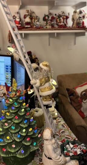 A figurine of a Black Santa in a gold suit climbing a ladder.