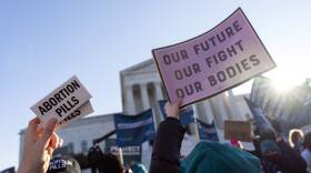 A crowd of protesters hold signs in front of the Supreme Court of the United States. Signs read "abortion pills" and "our future, our fight, our bodies"