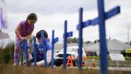 Two young children push blue crosses into the grass next to a road that remains closed with police barricades.
