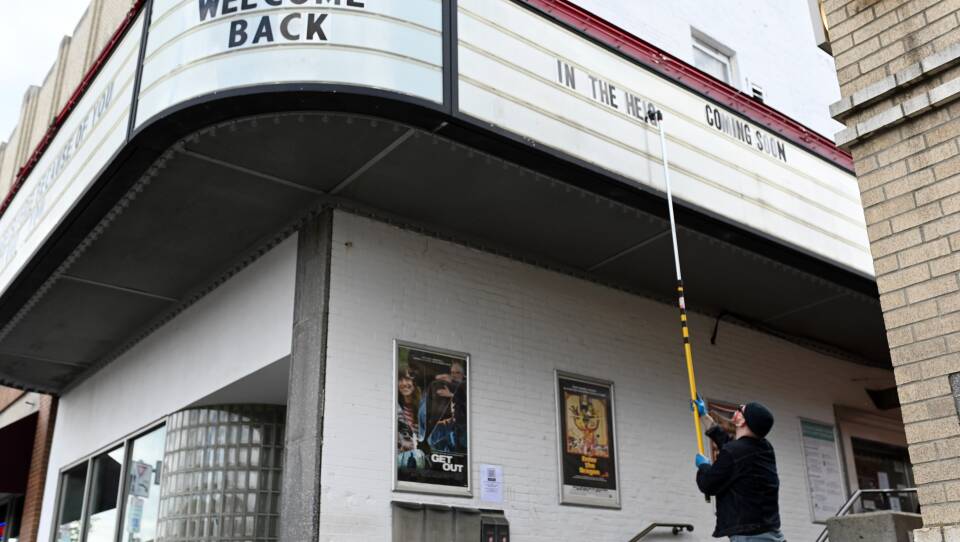 A person uses a long pole to change the letters on the sign outside a movie theater.