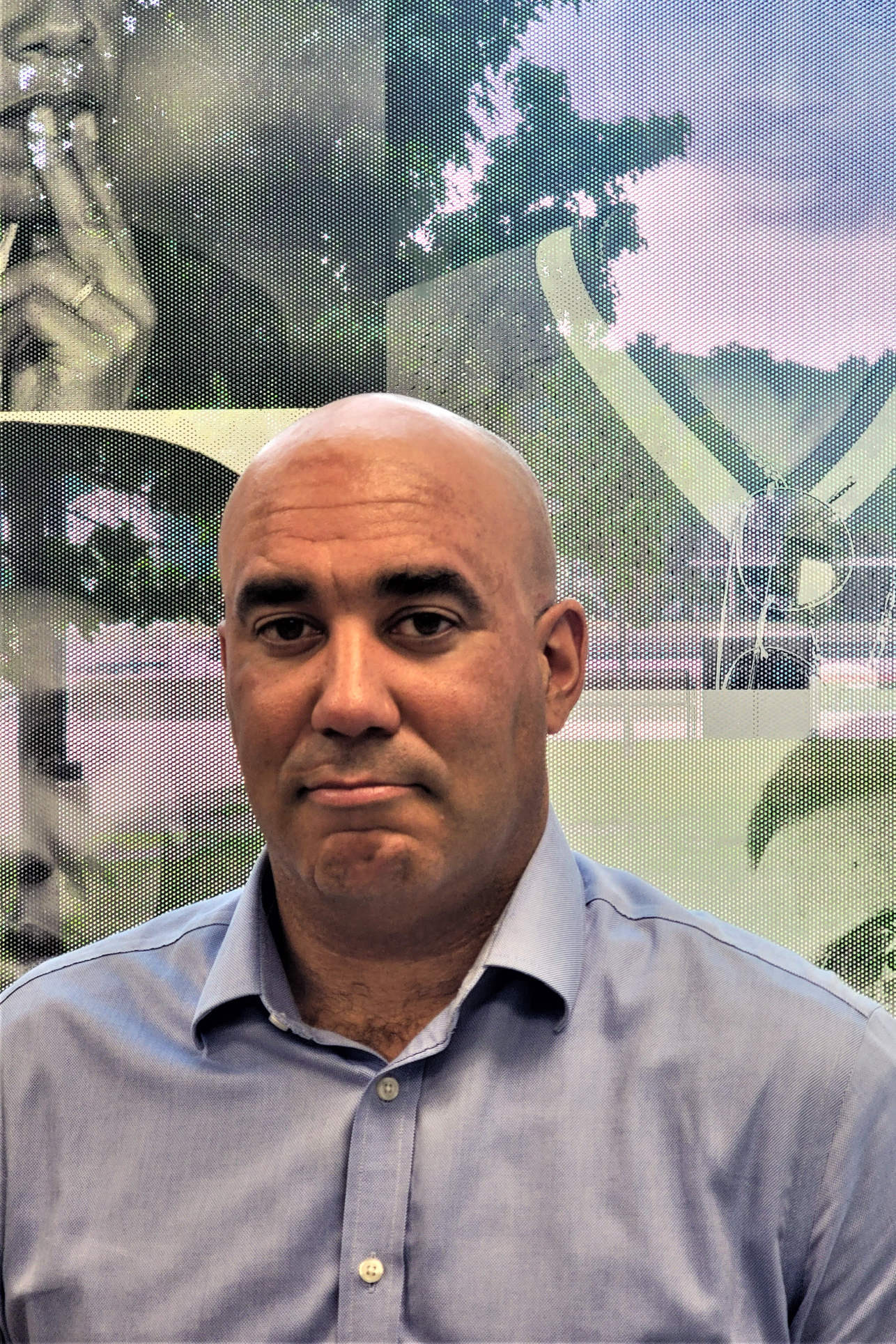 A bald man in a buttondown shirt looks seriously into the camera