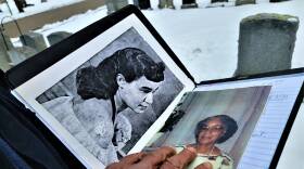 A man's hand rests atop two photos of a woman that he has in a folder. One is black-and-white photo of a young woman and a color photo of an old woman.