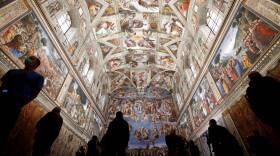 People walk underneath the intricately detailed mural ceiling of the Sistine Chapel