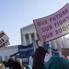 A crowd of protesters hold signs in front of the Supreme Court of the United States. Signs read "abortion pills" and "our future, our fight, our bodies"
