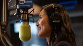 An Asian American woman wears headphones and speaks into a studio microphone.