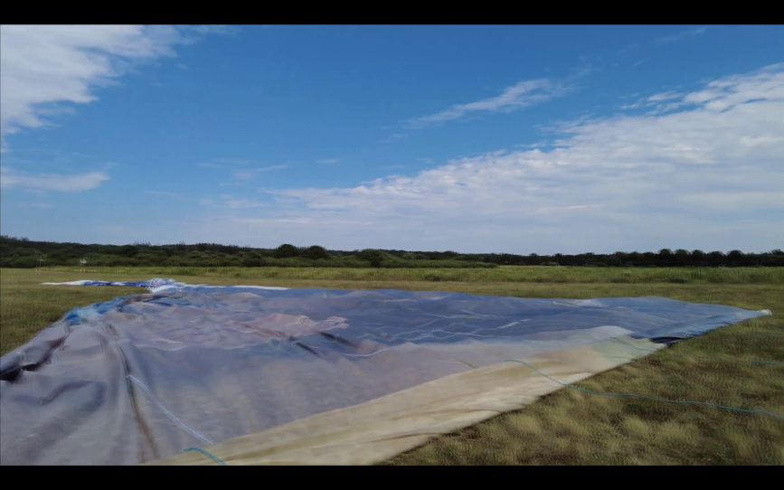 An airplane billboard, which is mostly white and blue, covers a huge expanse of ground at the Cape Cod Airfield Base, after it's been released from the banner plane and fallen to the ground.