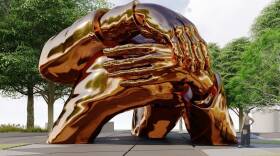 A large bronze sculpture of hands wrapped around each other sits in the center of a park.