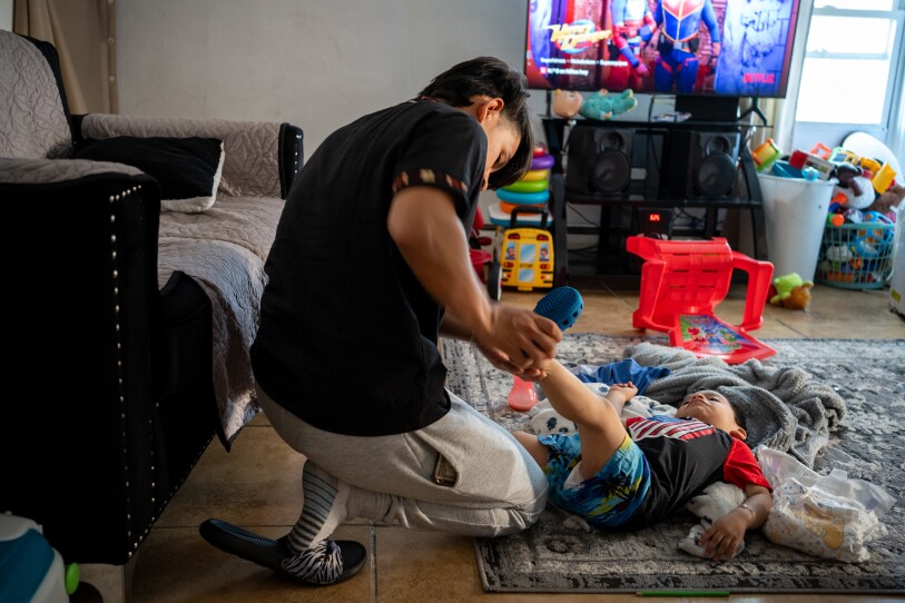 A teenager puts a Croc on a toddler in a living room