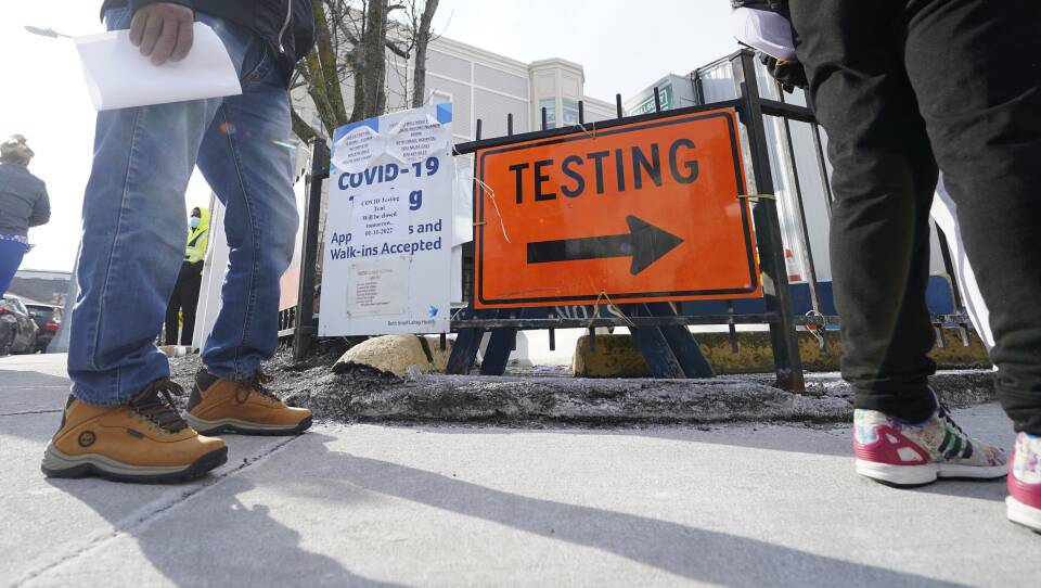 A low-angled photo shows peoples legs as they stand on a sidewalk by a large orange sign reading "testing"