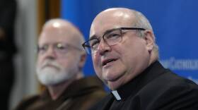 Two older men in cassocks at a press conference.