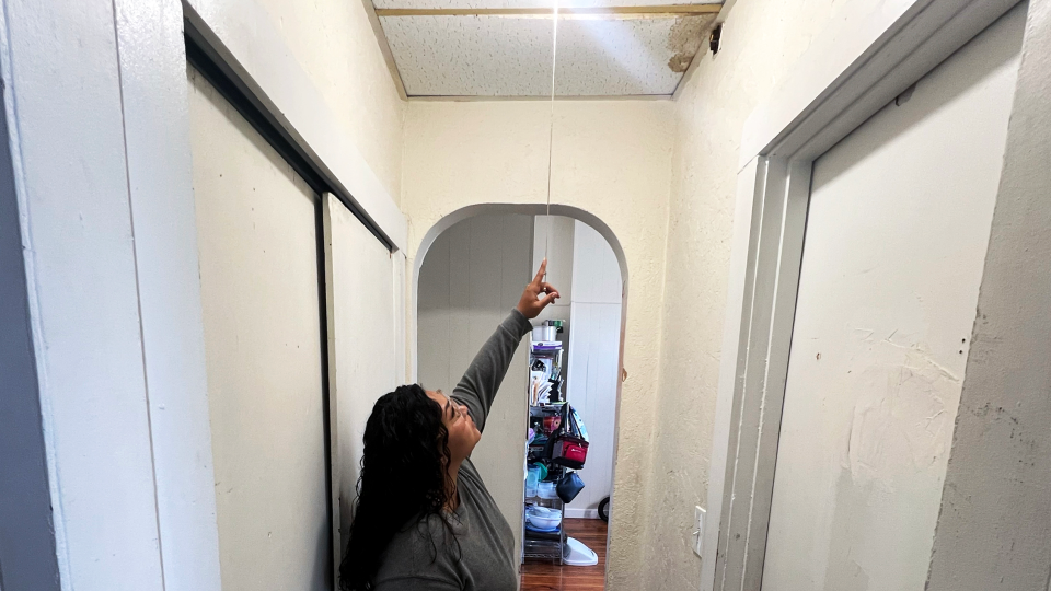A lady stands in her apartment pointing to her ceiling