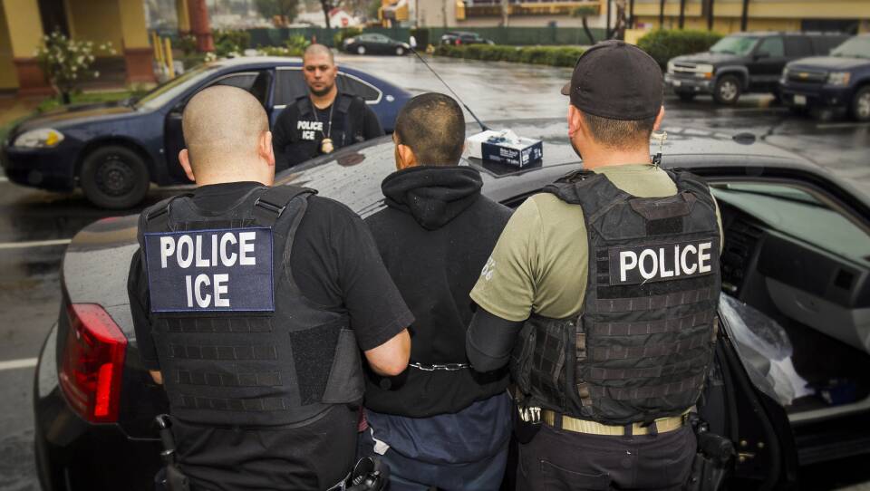 Two police officers arrest a man in a hoodie.