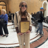 A woman wearing sunglasses holds a white and a bronze plaque.