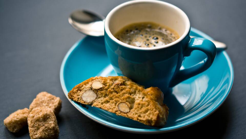 Cup of coffee with biscotti and 3 sugar cubes.