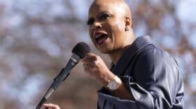 Pressley wears a black jacket and speaks into a microphone outside.