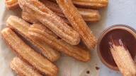 Plate with fluted churros coated in cinnamon sugar with one dipped into a bowl of chocolate sauce