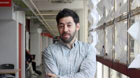 A man stands with his arms crossed in a school hallway.