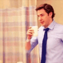 John Krasinski, as Jim in the Office, looks at the camera, crooks his eyebrow and frowns before taking a sip of coffee.
