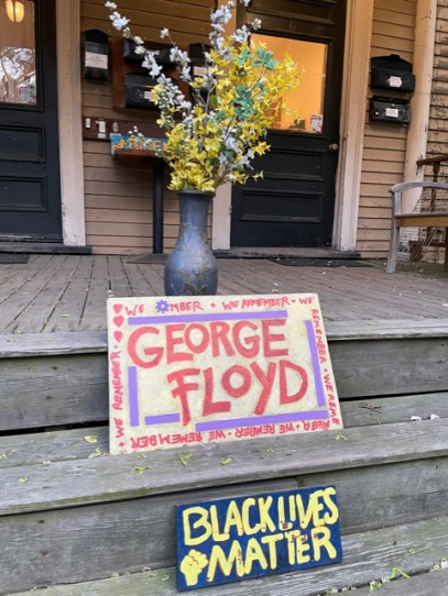 Two sings rest on a porch in front of a vase of flowers that read George Floyd and Black Lives Matter.