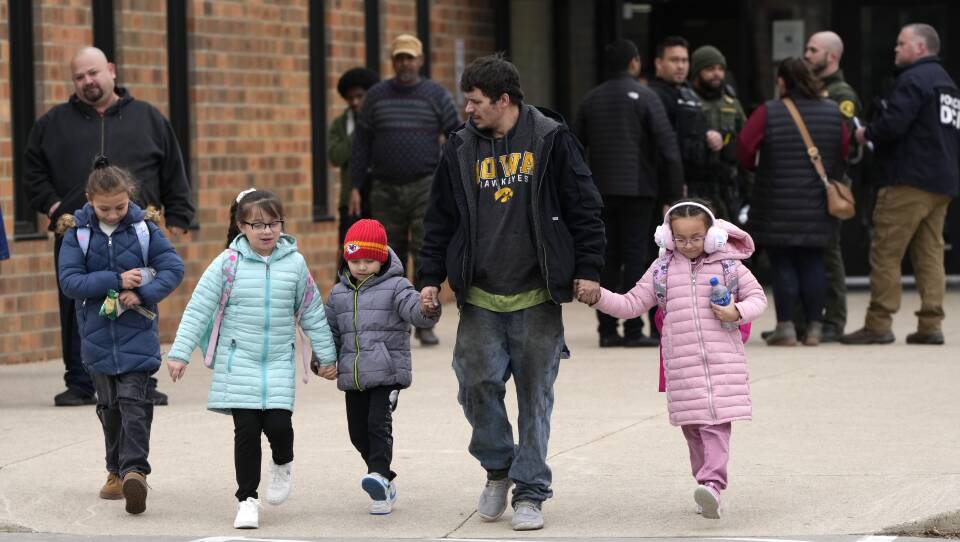 A man escorts four young children away from a school building, holding two of their hands