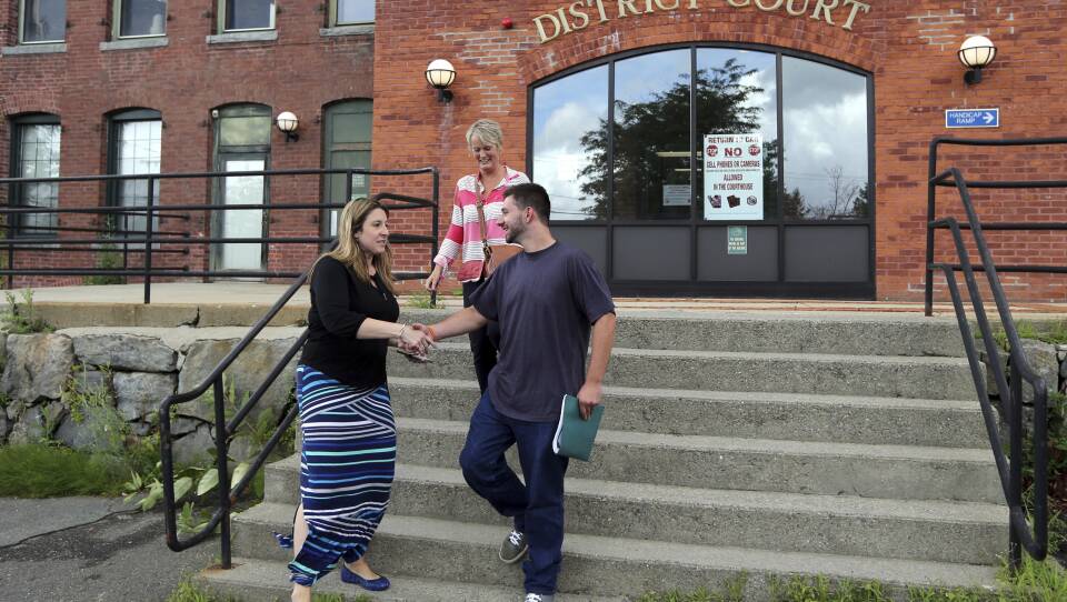 A man shakes hands with a woman at the base of a staircase outside a brick building, which has a large sign reading "Orange District Court."