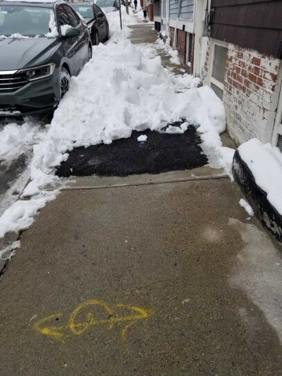 An impassable sidewalk is covered with snow with a narrow, slightly tamped down path over to the right close to the building.