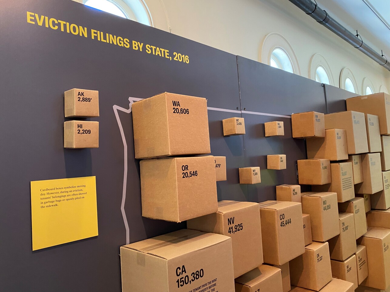Cardboard moving boxes of various sizes are fixed on a wall across an outline of the United States.