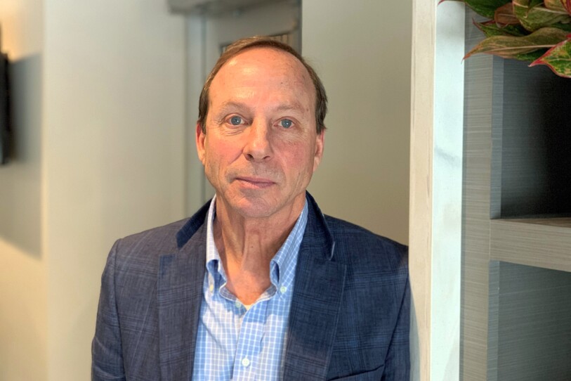 A man in a button-down shirt and a blazer looks directly into the camera with a straight face.