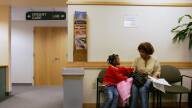 A mother and daughter sit in a doctor's office waiting room.