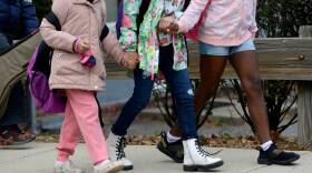 Three children hold hands as they walk along a sidewalk.