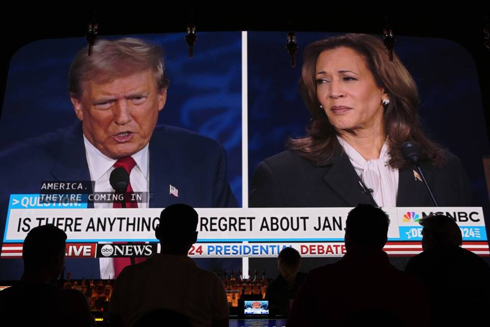 Several people at a bar watch Donald Trump and Kamala Harris debate on a giant TV screen.